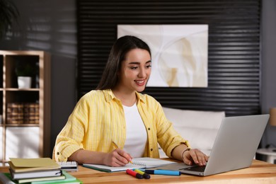 Young woman watching webinar at table in room