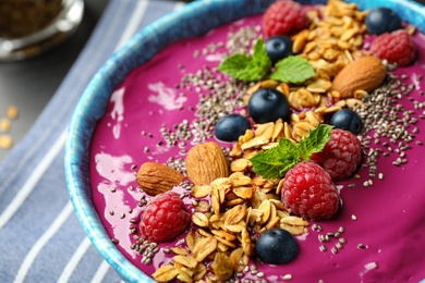 Photo of Delicious acai smoothie with granola and berries in dessert bowl served on table, closeup