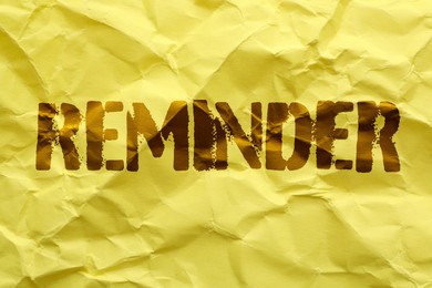 Word REMINDER written on crumpled yellow paper