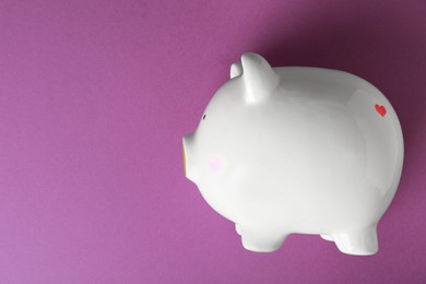 Photo of Ceramic piggy bank on purple background, top view. Space for text