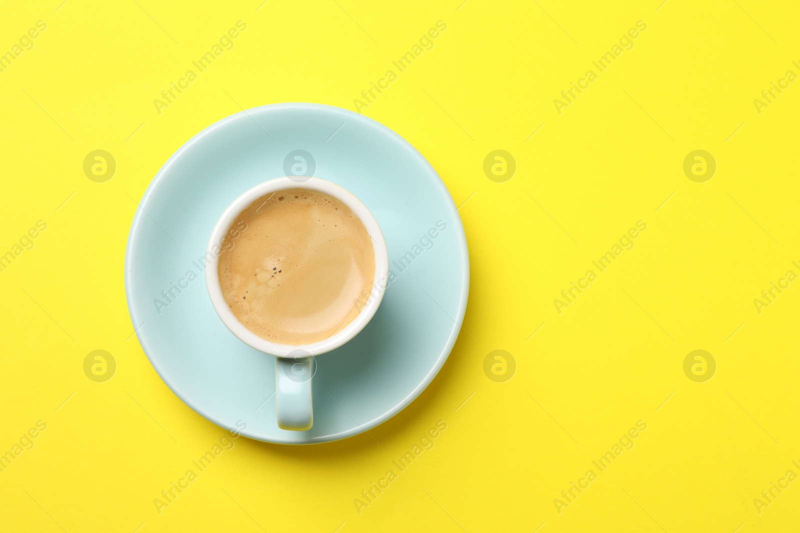 Photo of Aromatic coffee in cup on yellow background, top view. Space for text