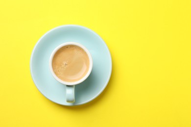 Photo of Aromatic coffee in cup on yellow background, top view. Space for text