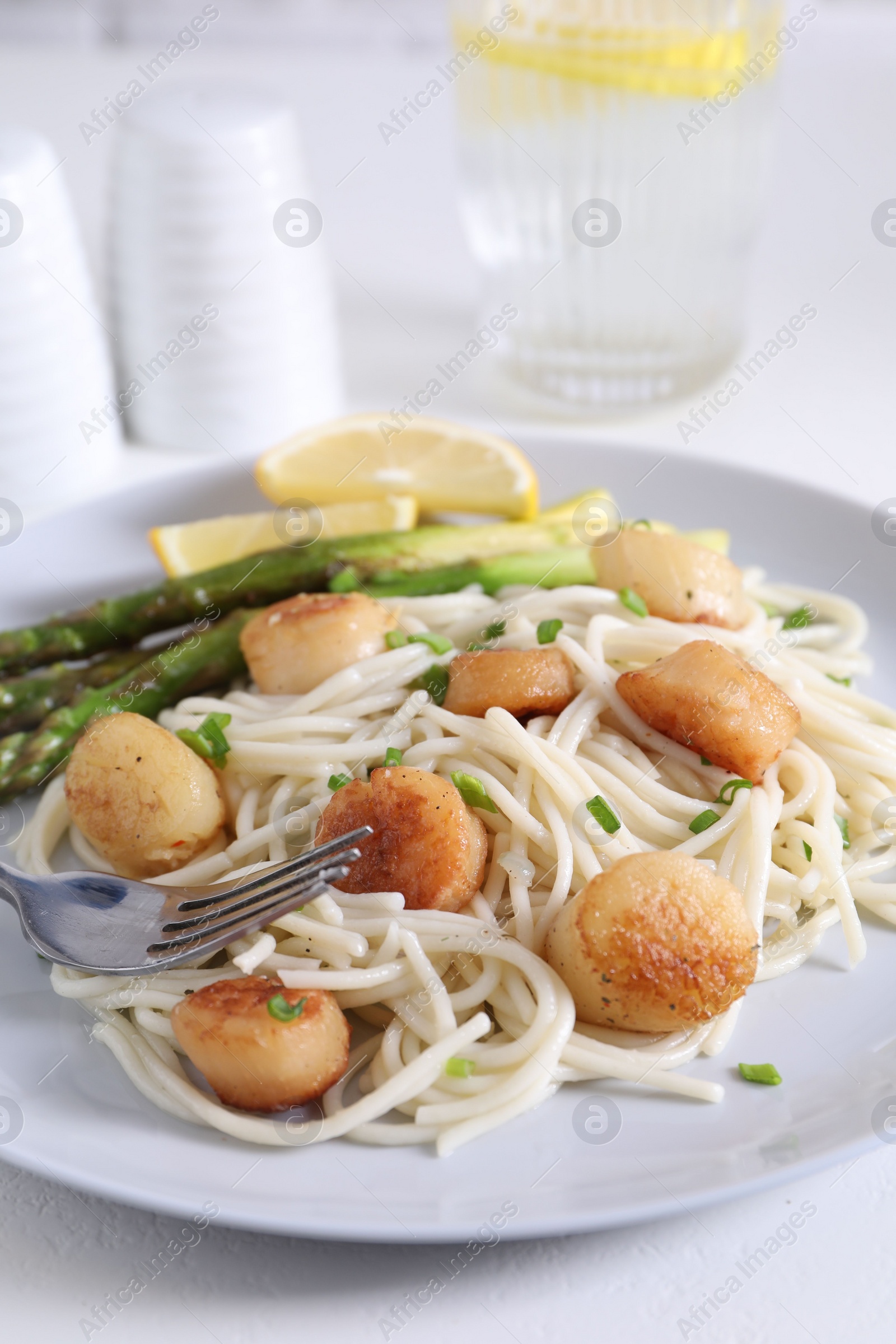 Photo of Delicious scallop pasta with asparagus, green onion and lemon served on white table, closeup