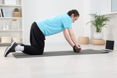Photo of Senior man in sportswear doing exercises near laptop on fitness mat at home