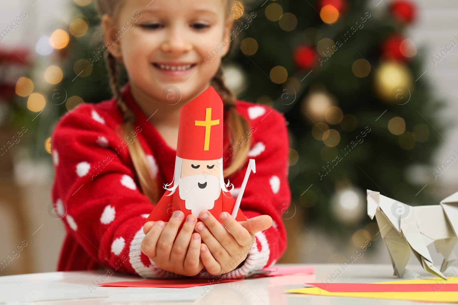 Photo of Cute little girl with paper Saint Nicholas toy at home, focus on hands