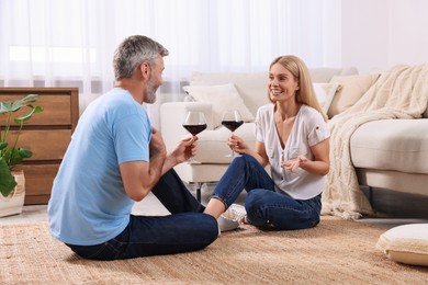 Photo of Happy affectionate couple with glasses of wine on floor at home. Romantic date