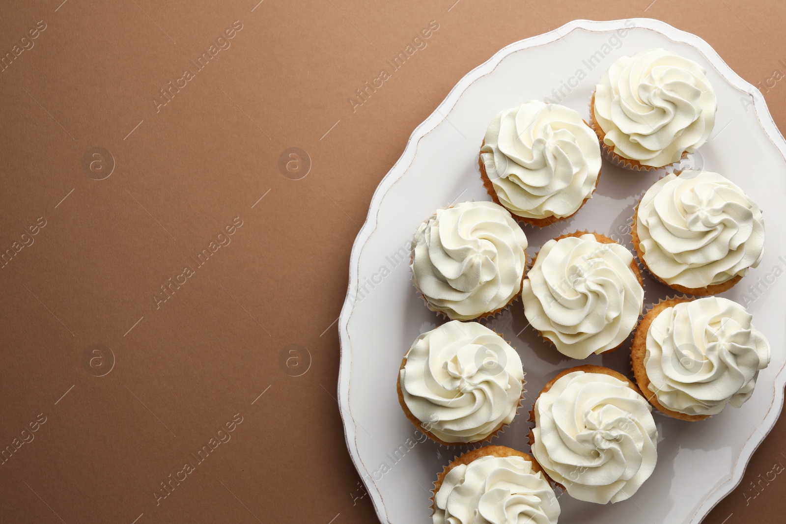 Photo of Tasty vanilla cupcakes with cream on dark beige background, top view. Space for text