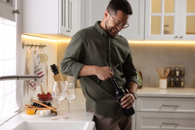 Photo of Romantic dinner. Man opening wine bottle with corkscrew in kitchen