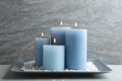 Plate with burning color candles and rocks on table