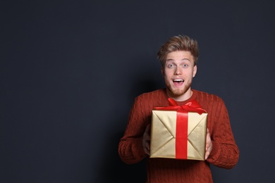 Emotional young man with Christmas gift on dark background. Space for text