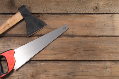 Photo of Saw with colorful handle and axe on wooden background, flat lay. Space for text