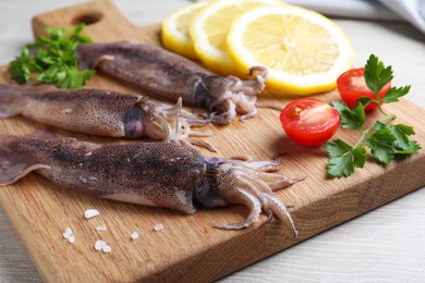 Photo of Fresh raw squids with lemon, parsley and tomato on white wooden table, closeup