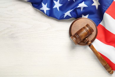Photo of Judge's gavel and American flag on white wooden table, flat lay. Space for text