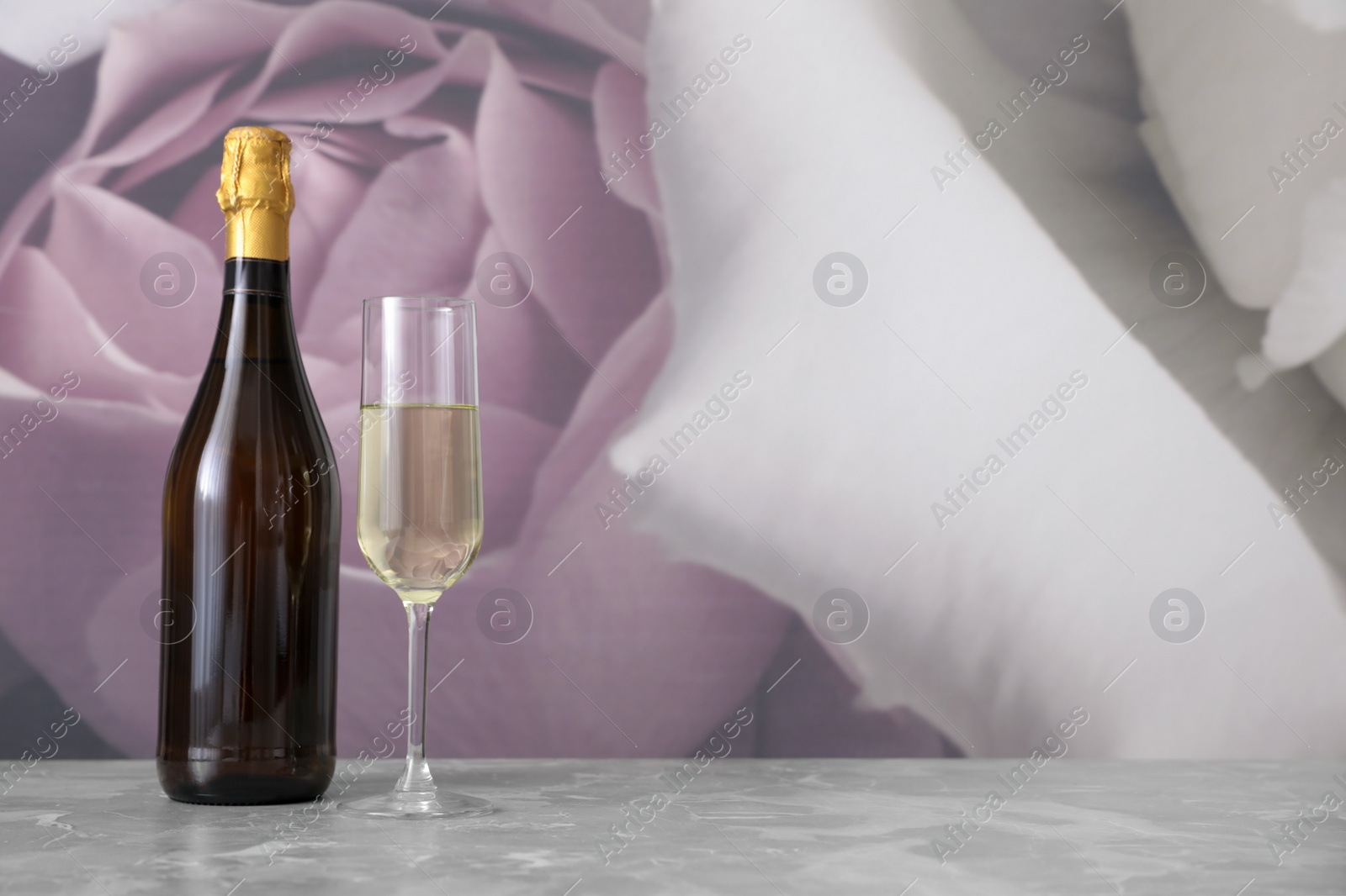 Photo of Bottle and glass of champagne on grey table. Space for text