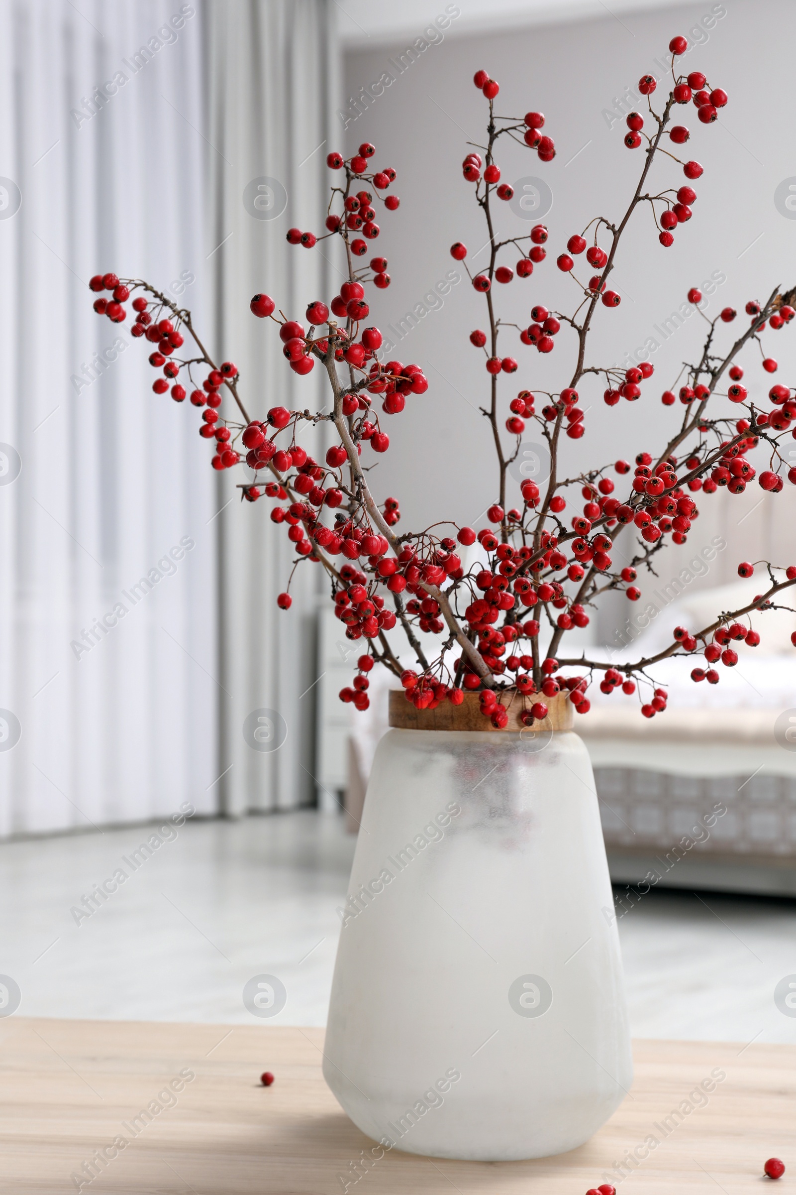 Photo of Hawthorn branches with red berries on wooden table in bedroom