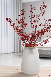 Hawthorn branches with red berries on wooden table in bedroom