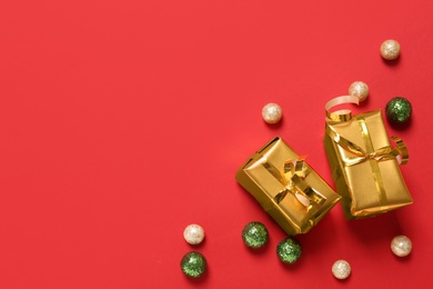 Gift boxes and Christmas balls on red background, flat lay. Space for text