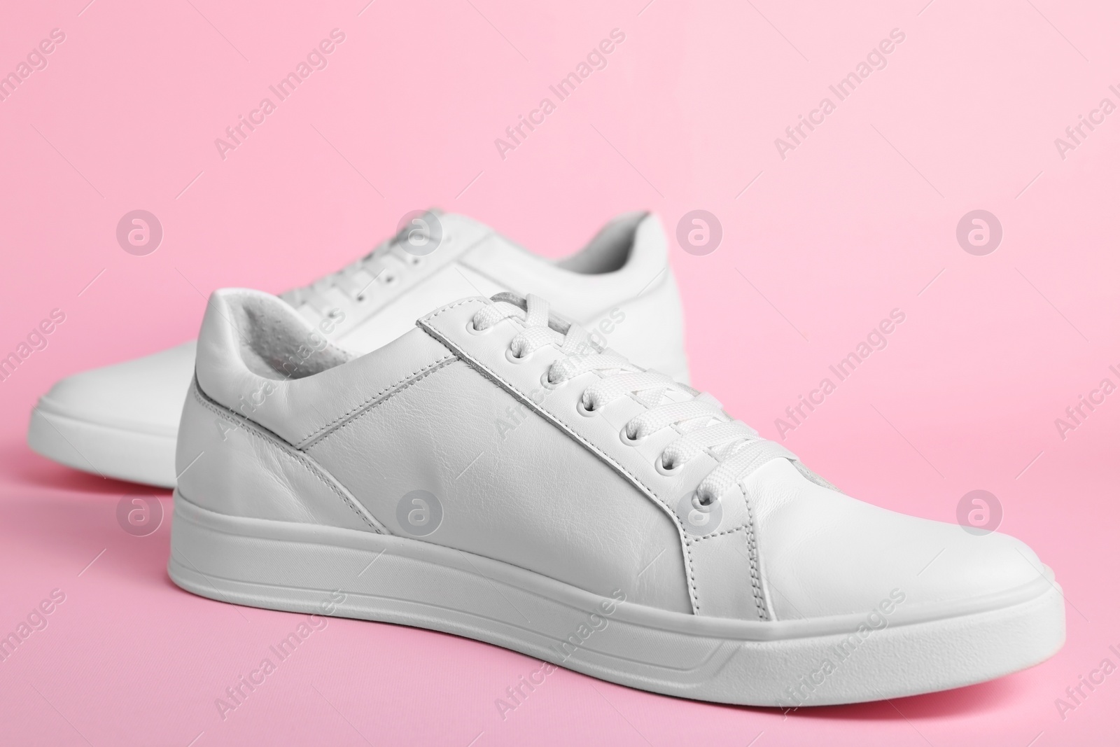 Photo of Pair of stylish white sneakers on pink background