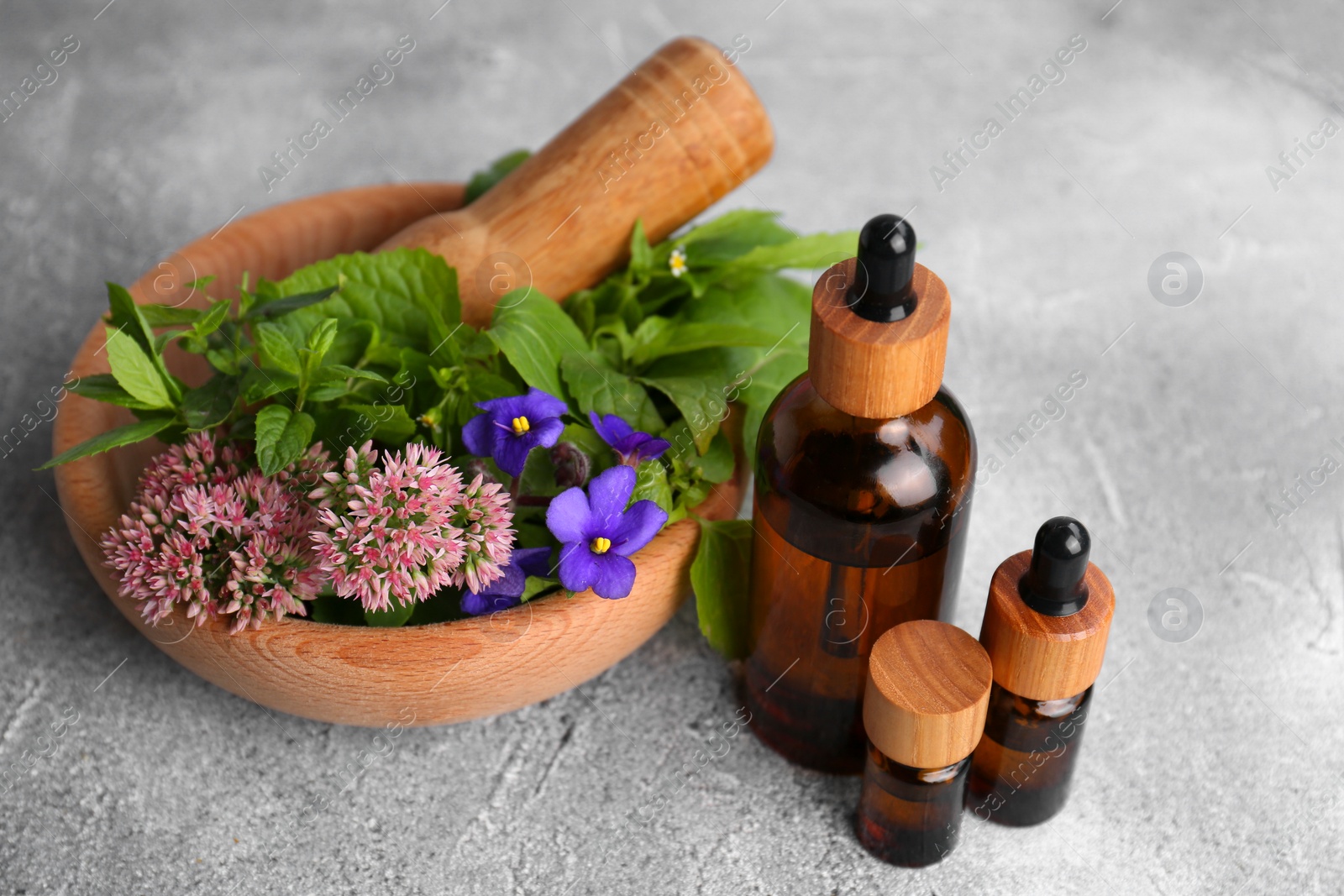 Photo of Glass bottles of essential oil and mortar with different wildflowers on light grey table