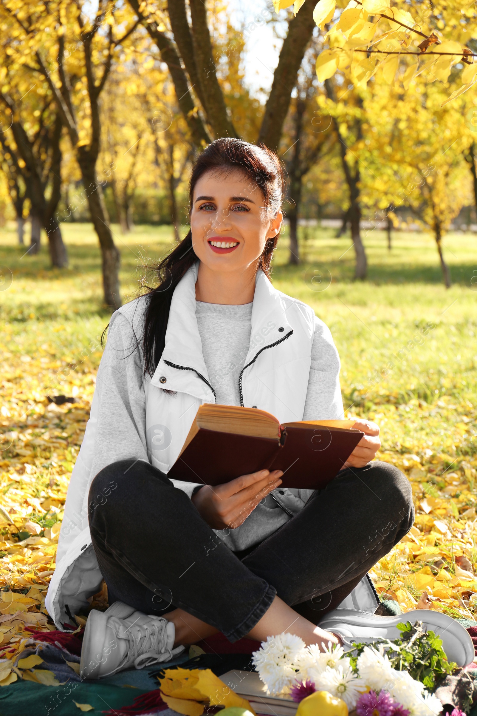 Photo of Happy woman reading book in park on autumn day