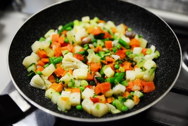 Frying pan with mix of vegetables on kitchen stove, closeup