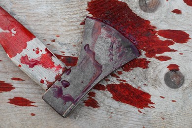 Axe with blood on wooden surface, top view