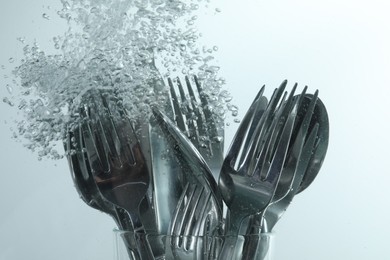 Photo of Washing silver cutlery in water on white background, closeup