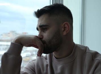 Photo of Portrait of sad man near window at home