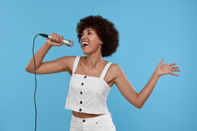 Curly young woman with microphone singing on light blue background