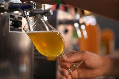 Bartender pouring cold tasty beer into glass in pub, closeup