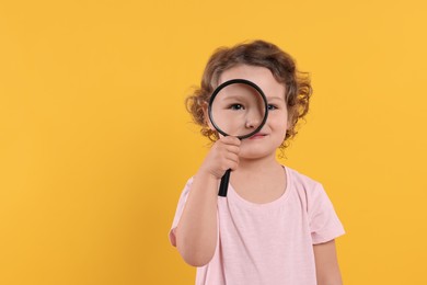 Cute little girl looking through magnifier glass on orange background, space for text. Searching concept