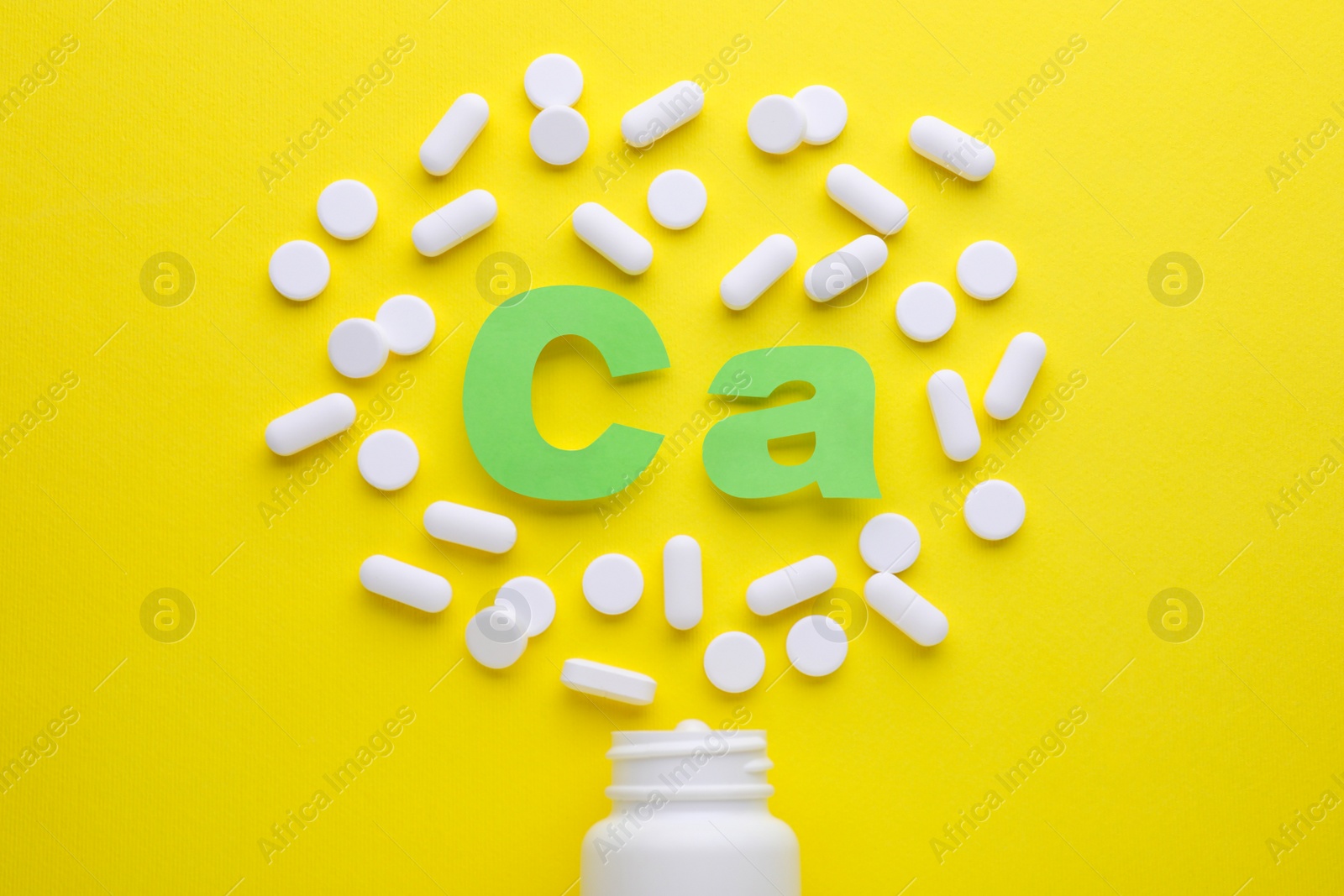 Photo of Pills, open bottle and calcium symbol made of green letters on yellow background, flat lay