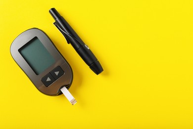 Digital glucometer and lancet pen on yellow background, flat lay with space for text. Diabetes control