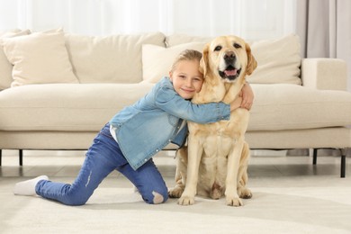 Photo of Cute child hugging her Labrador Retriever on floor at home. Adorable pet