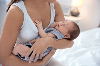Young woman holding her baby near breast in bedroom, closeup