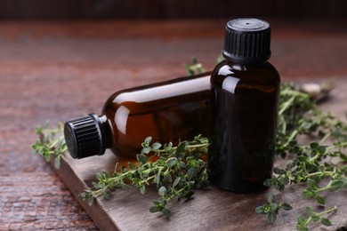 Photo of Bottles of thyme essential oil and fresh plant on wooden table, closeup