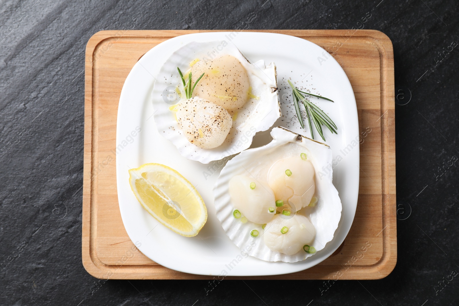 Photo of Raw scallops with green onion, rosemary and lemon on dark textured table, top view