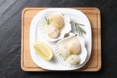 Photo of Raw scallops with green onion, rosemary and lemon on dark textured table, top view