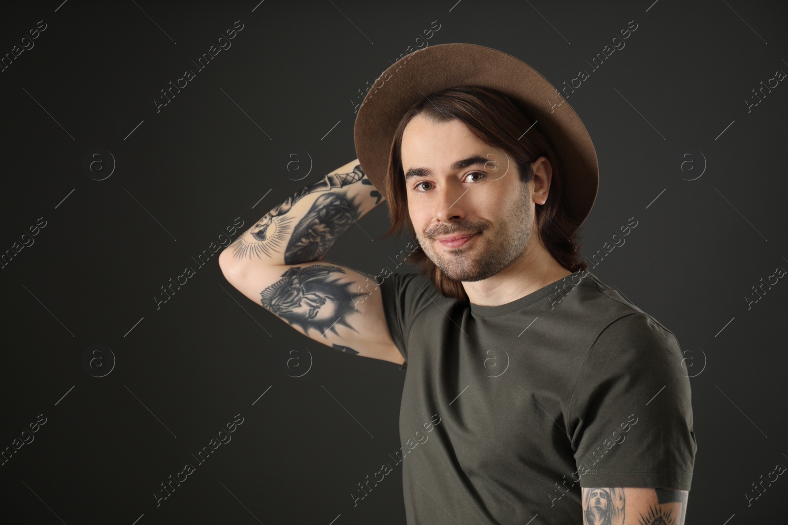 Photo of Young man with tattoos on arms against black background