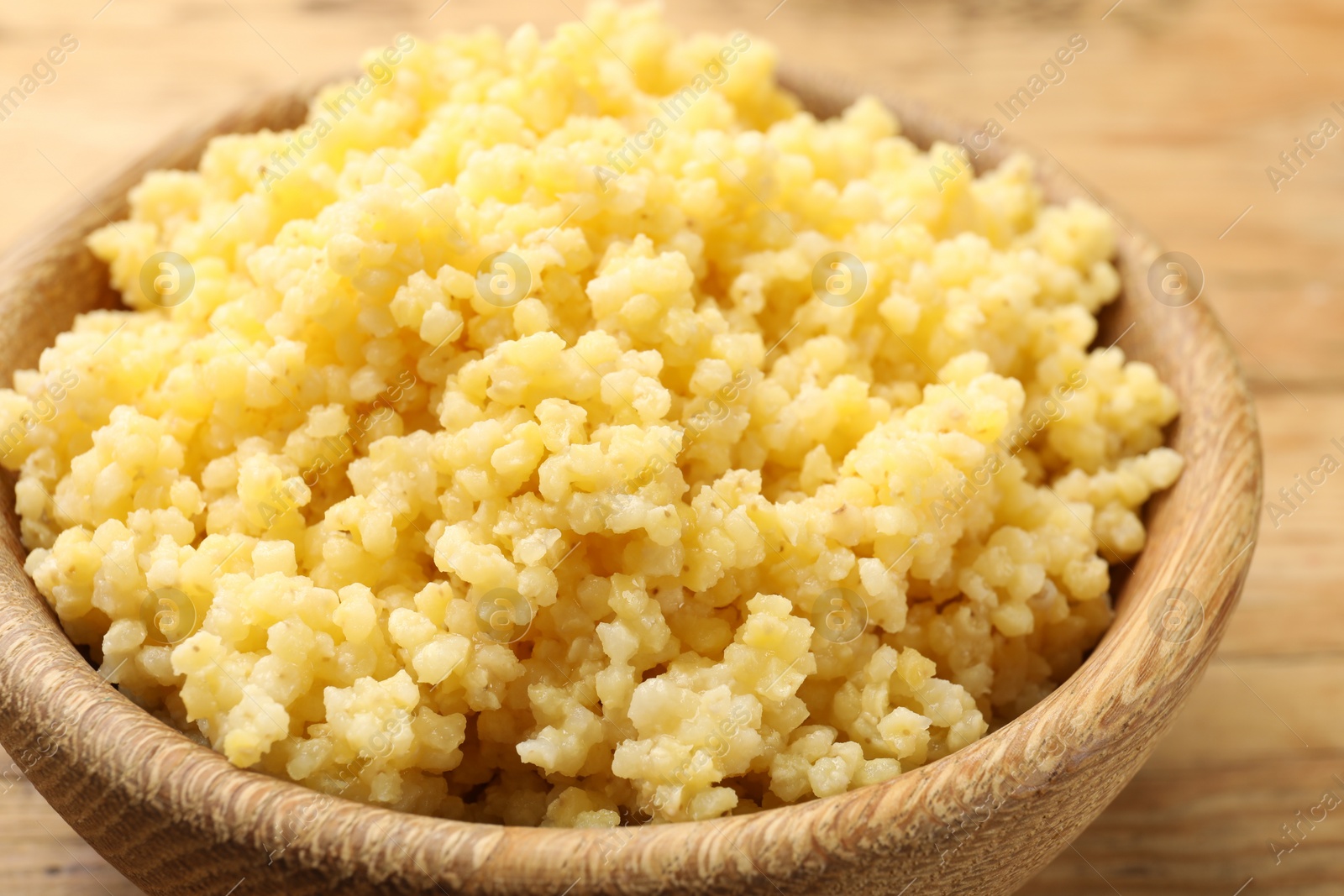 Photo of Tasty millet porridge in wooden bowl on table, closeup