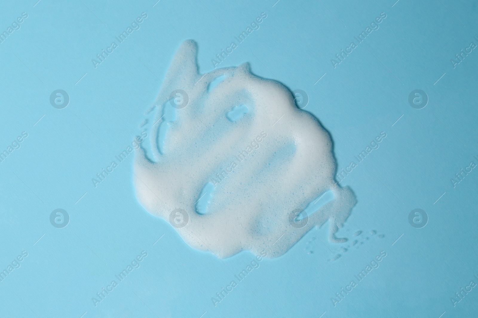 Photo of Foam on light blue background, top view. Face cleanser, skin care cosmetic