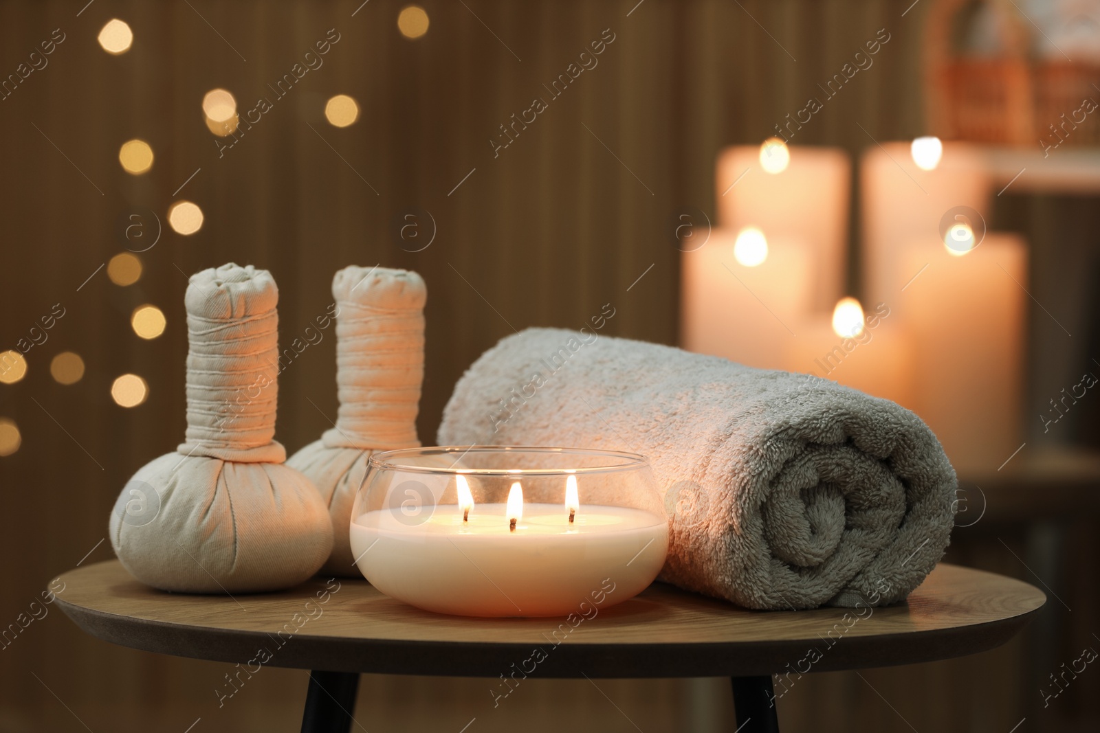 Photo of Spa composition. Herbal bags, towel and burning candle on wooden table