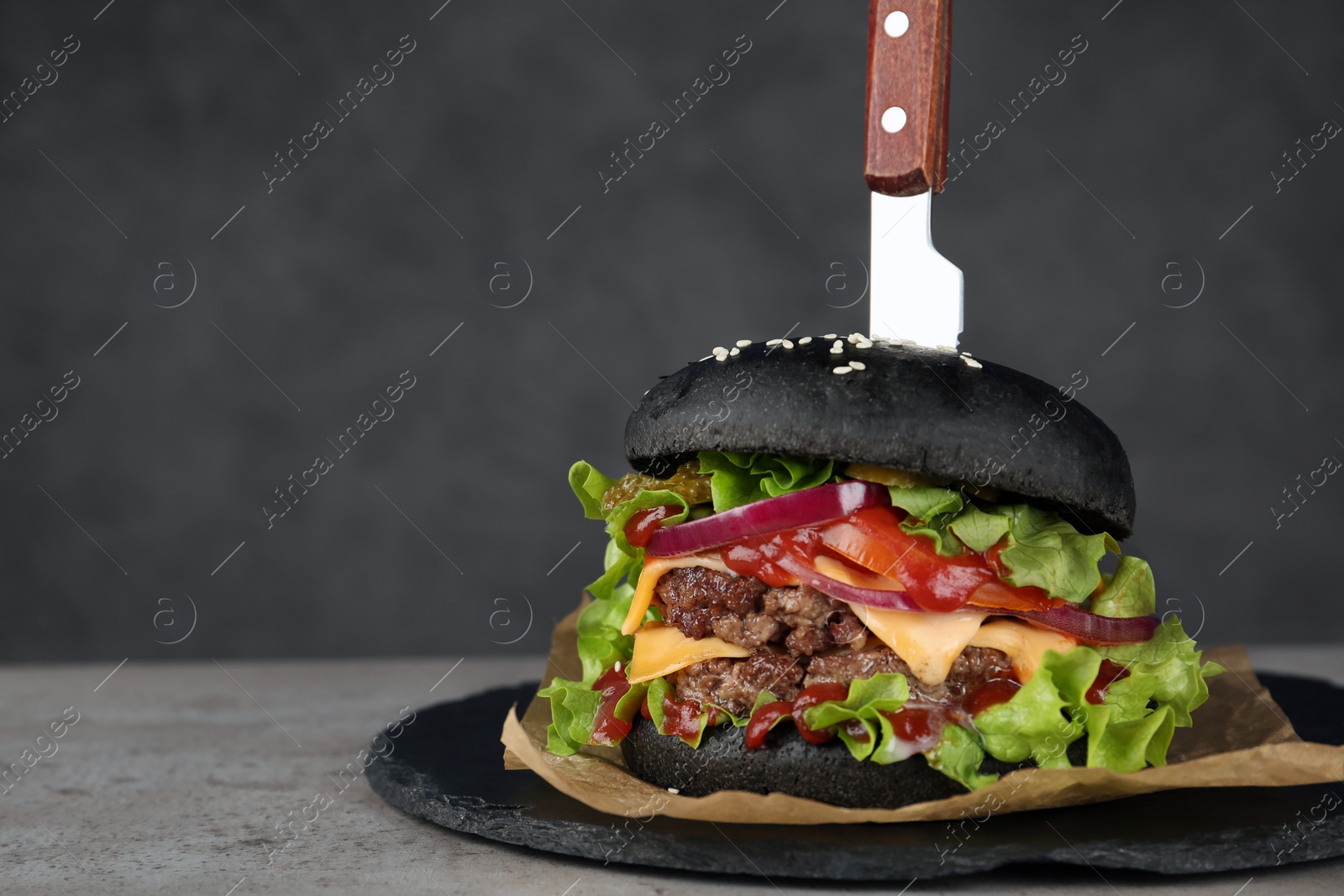 Photo of Slate plate with black burger on table. Space for text