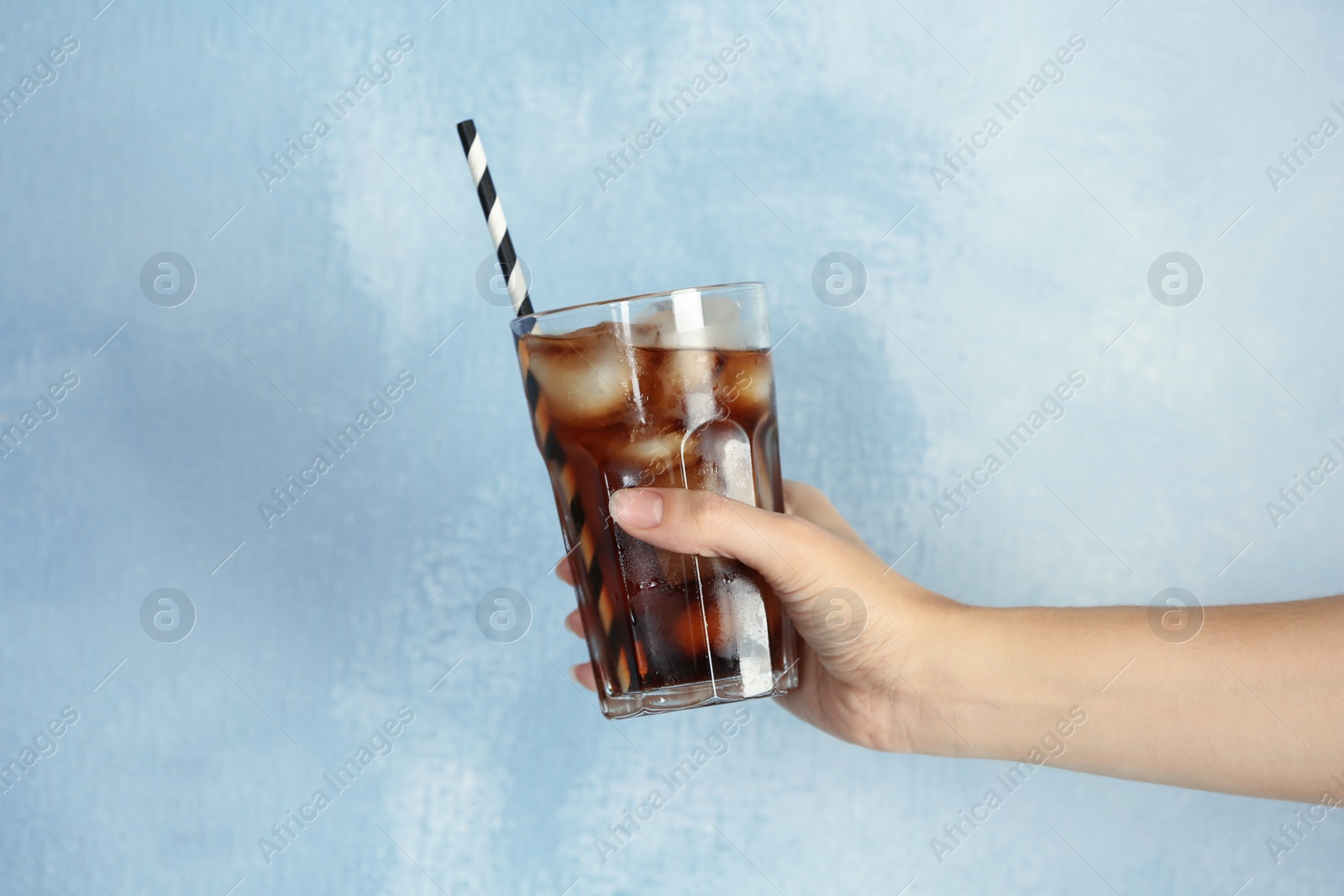Photo of Woman holding glass of tasty refreshing cola with ice cubes on color background, closeup view