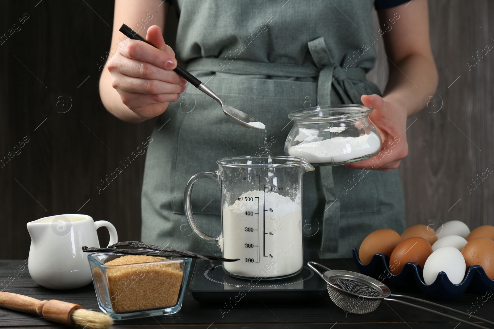 Photo of Woman adding baking powder into measuring cup at black wooden table, closeup