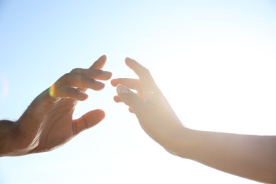 Photo of Man and woman reaching hands to each other against blue sky, closeup. Nature healing power