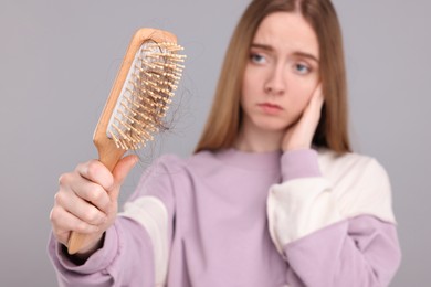 Woman holding brush with lost hair on light grey background, selective focus. Alopecia problem