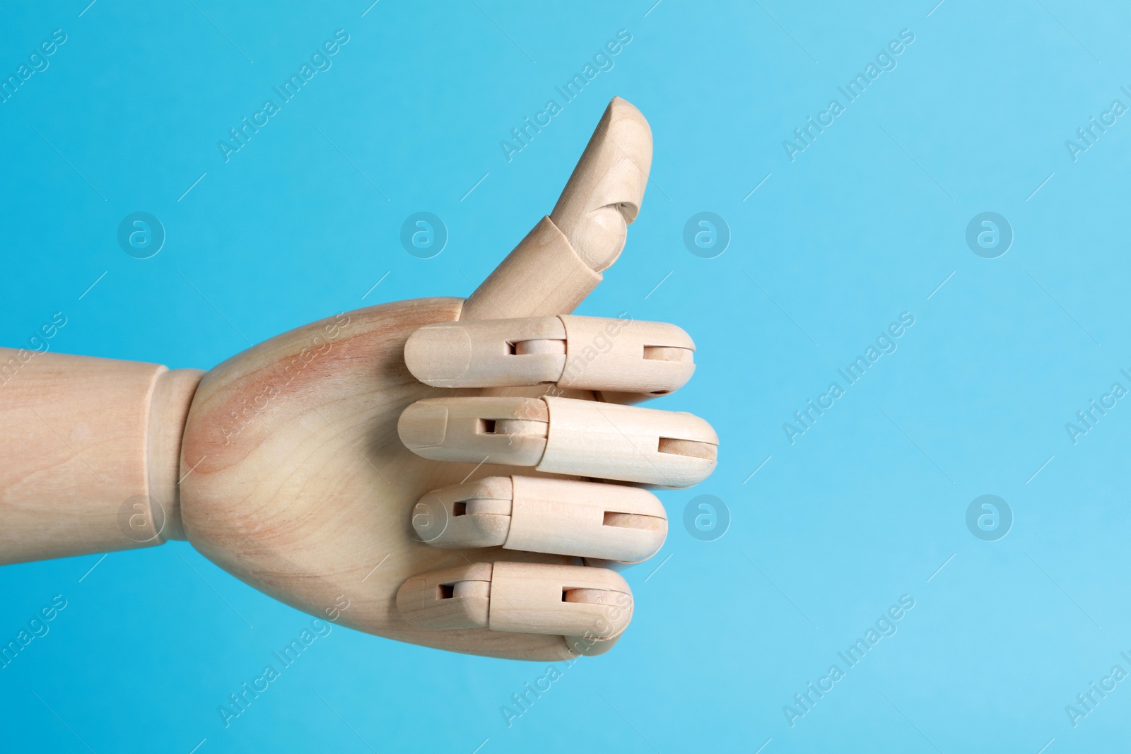 Photo of Wooden mannequin hand showing thumb up on light blue background. Space for text