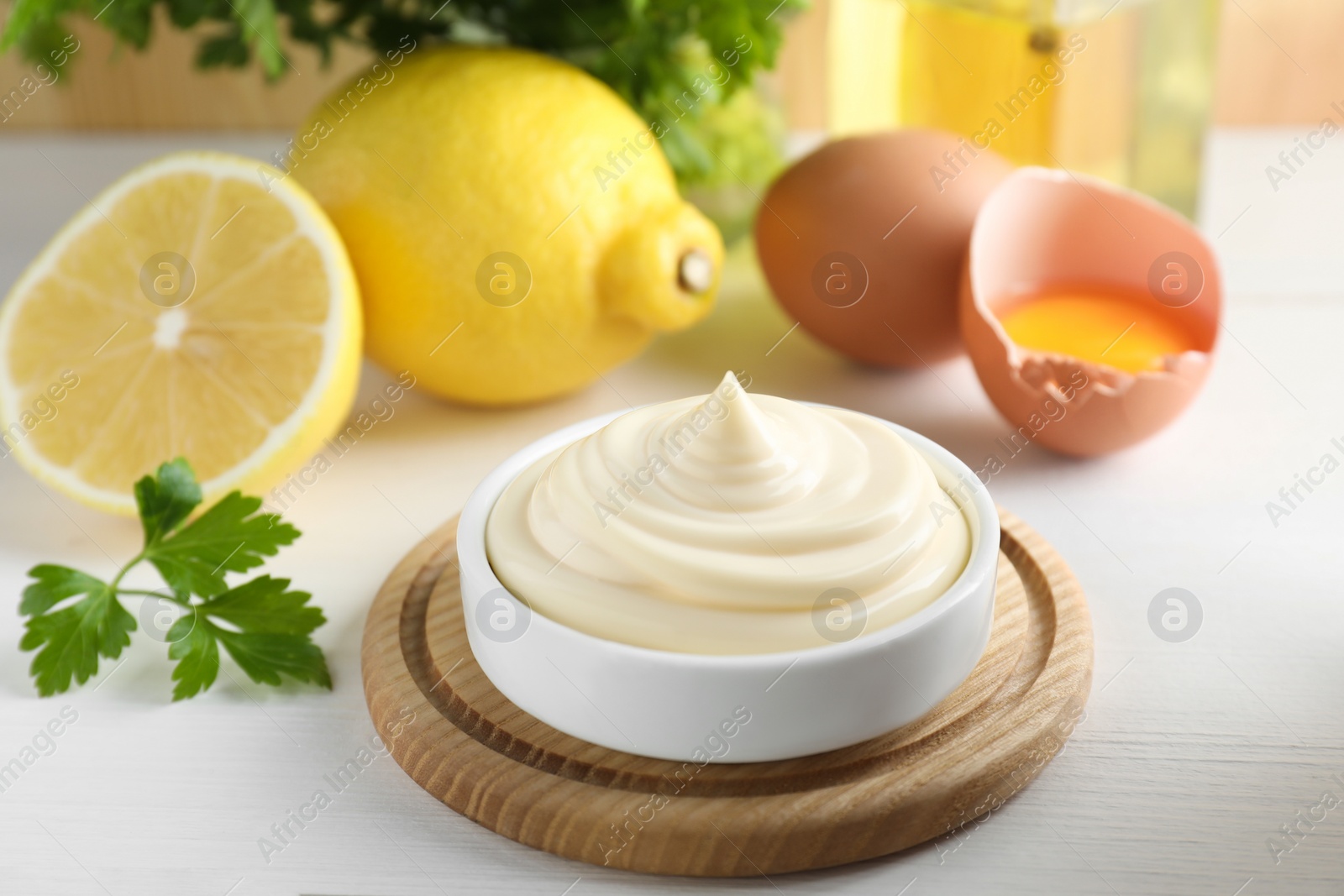 Photo of Fresh mayonnaise sauce in bowl and ingredients on white wooden table, closeup