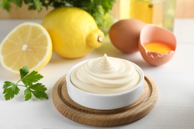 Fresh mayonnaise sauce in bowl and ingredients on white wooden table, closeup